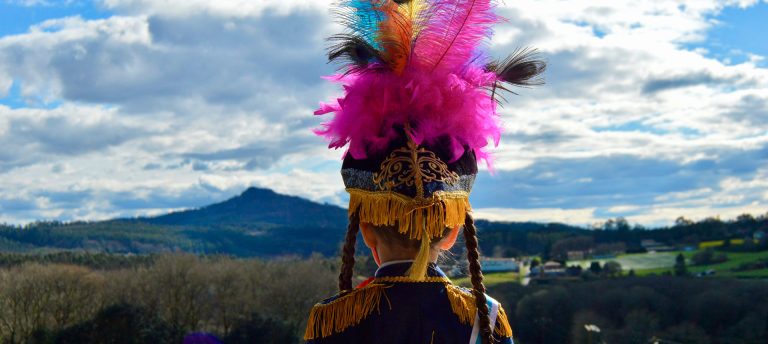 Danzante de costas cun penacho de plumas de cores mirando cara ao Pico Sacro